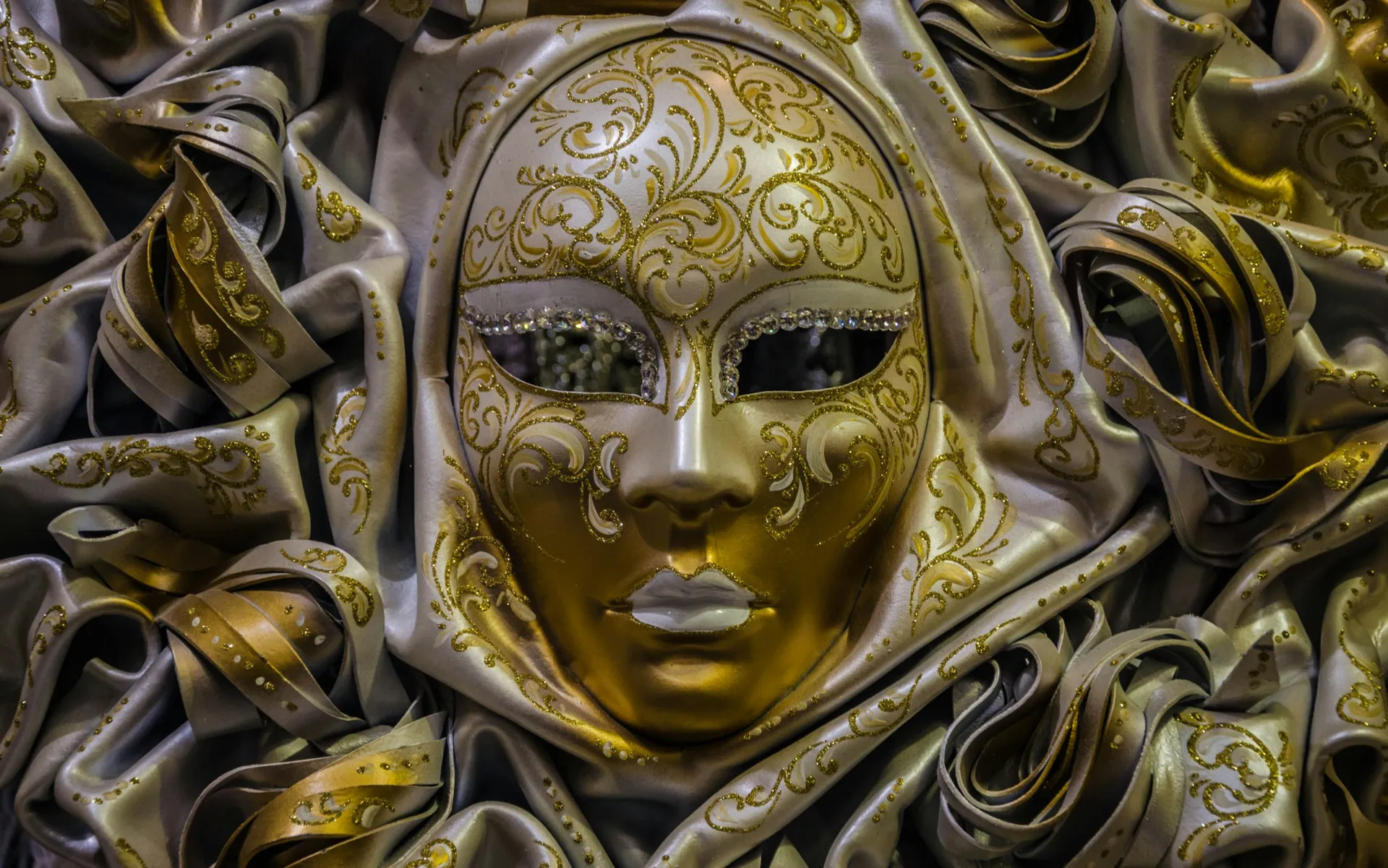 A gold Venetian mask resting on folds of gold fabric